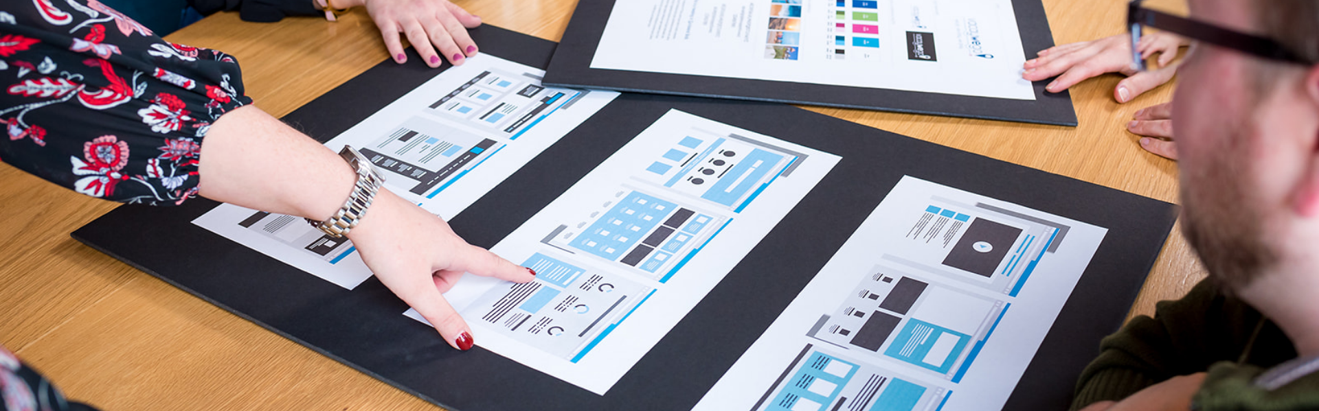 Hands pointing to a website wireframe on a conference table