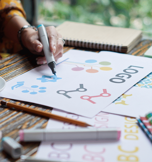 view of a hand drawing some logo sketches in a notebook.