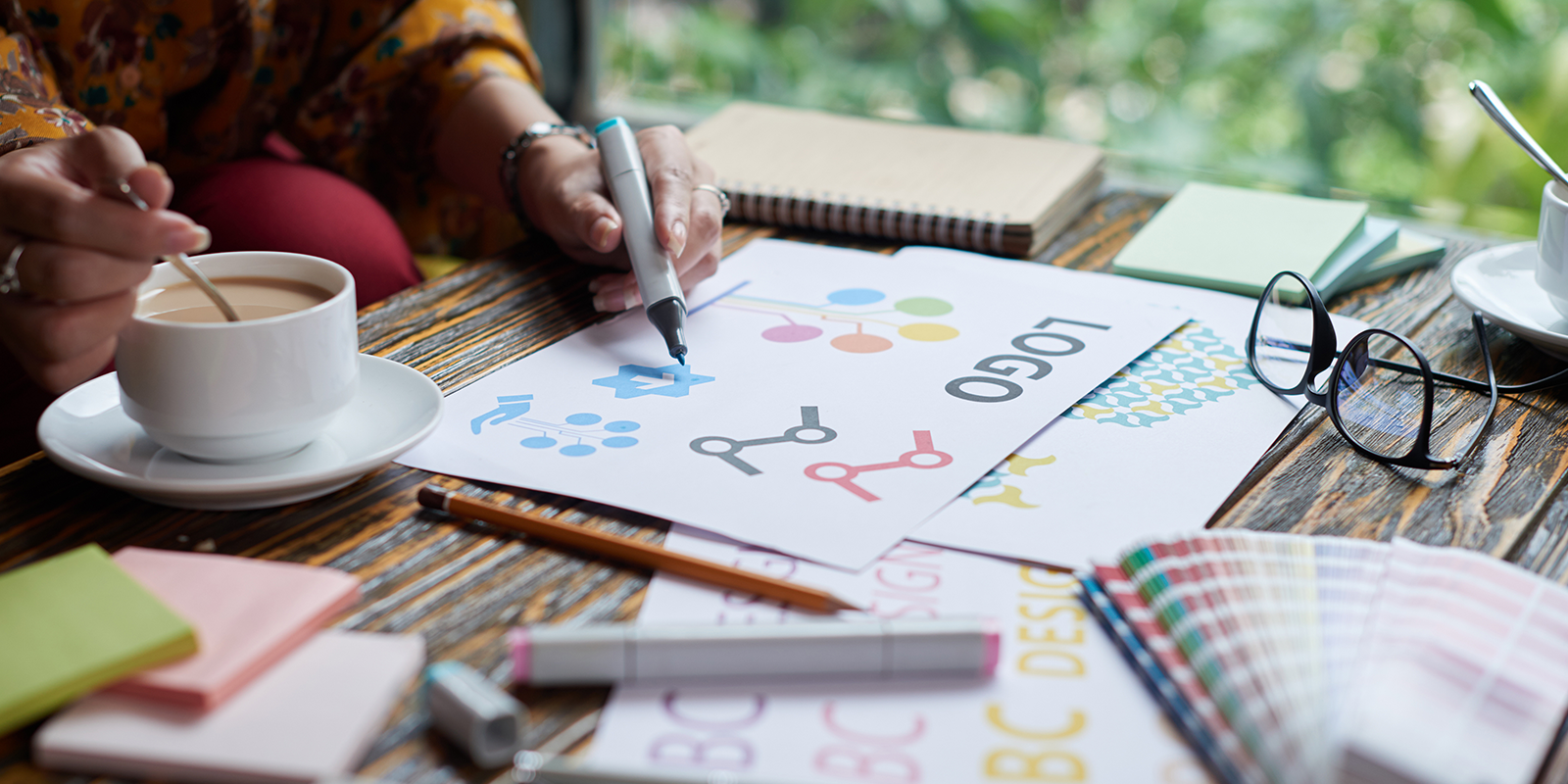 view of a hand drawing some logo sketches in a notebook.